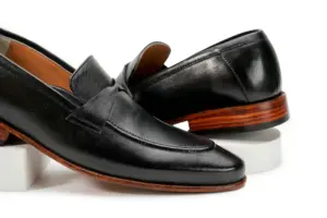 Close angled view of black leather swirl-strap loafers and apron stitching
