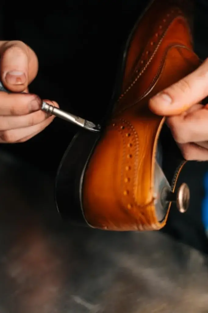 Shoemaker applying finish with a brush to the heel and sole edge of a brown leather shoe