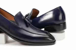 Close angled pair view of purple-black patina tassel loafers and apron stitching