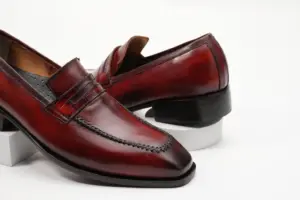Close angled view of red-burgundy patina penny loafers and apron stitching