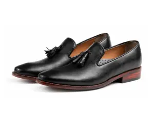 Pair of black aniline wholecut tassel loafers showing the tapered toes and brown sole edges