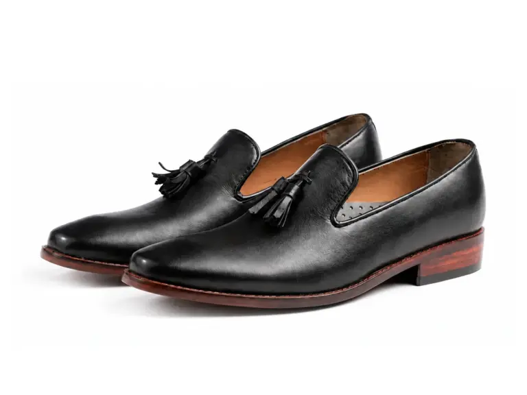 Pair of black aniline wholecut tassel loafers showing the tapered toes and brown sole edges
