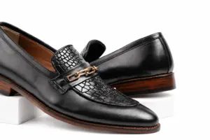 Close view of warm-toned chain and glossy croc-pattern apron on black leather loafers