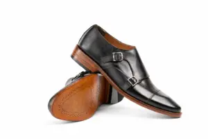 Angled pair of black cap-toe double monk straps showing leather sole