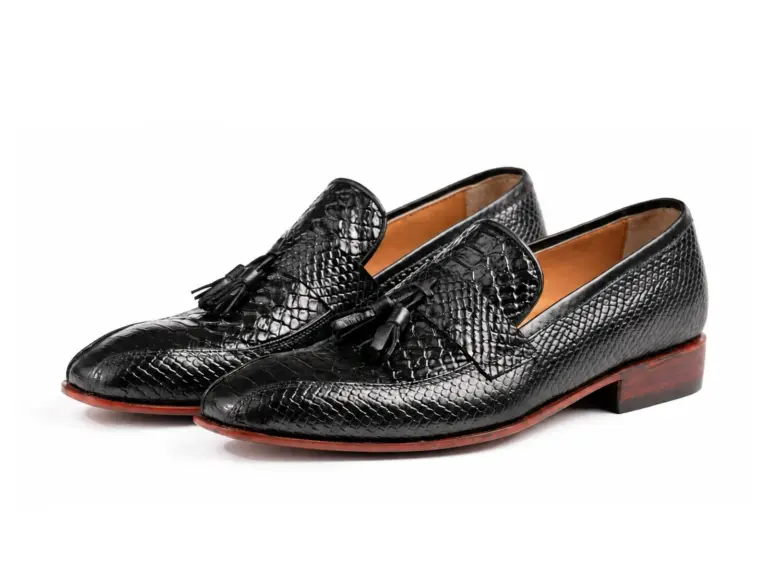 Three-quarter view of black patent-finish tassel loafers with reptile-pattern uppers