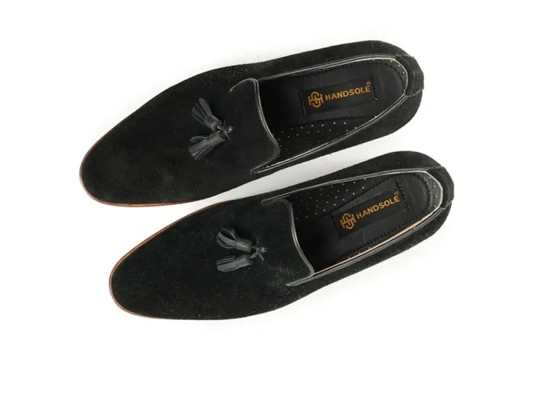 Existing overhead photo of black suede round-toe tassel loafers, rotated with toes toward the front-left and heels at the back-right.