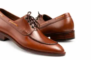Close-up of the hand-stitched apron seam and leather laces on a brown pull-up leather Derby