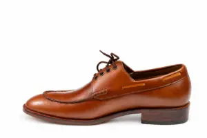 Side view of brown pull-up leather shoes: a moc toe Derby with stacked leather heel