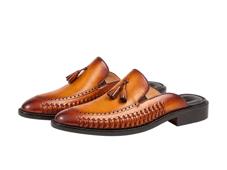 Three-quarter view of cognac tassel mules showing handwoven side panels and dark heel bases