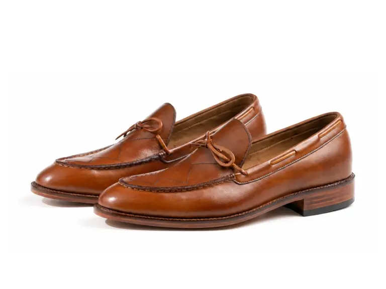 Pair of cognac criss-cross apron tie loafers on white background