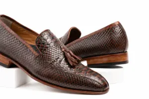 Three-quarter view of dark brown textured tassel loafers showing tassels and apron seam