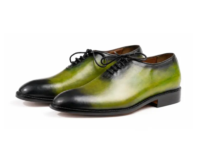 Pair of green-black patina wholecut Oxford shoes on white background