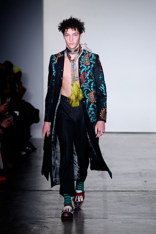 Model wearing Handsole burgundy footwear with a turquoise-patterned black runway coat