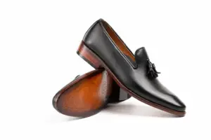 Crossed black tassel loafers showing a tapered forepart and brown leather underside