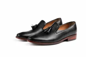 Pair of black aniline wholecut tassel loafers showing the tapered toes and brown sole edges