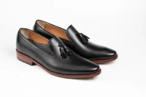 Three-quarter view of black leather wholecut loafers with tassels and layered brown heels