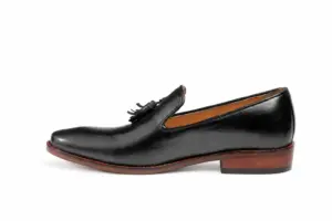 Side profile of a black wholecut tassel loafer showing the continuous upper and brown heel