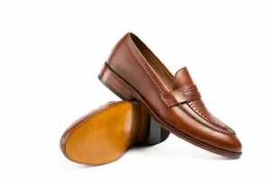 Crossed brown pull-up leather penny loafers showing the upper, outsole and heel