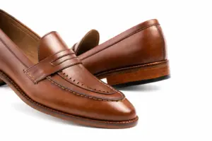 Close-up of brown pull-up leather penny loafers showing cut-out penny strap, perforated apron border and brown leather grain