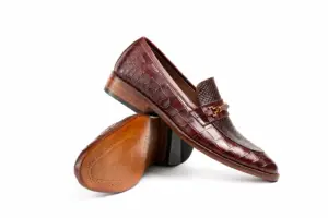 Crossed burgundy reptile-pattern horsebit loafers showing the upper, outsole and heel