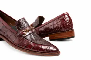Close-up of burgundy reptile-pattern horsebit loafers showing gold-tone bit-style hardware, lizard-pattern vamp and larger croc-pattern scales