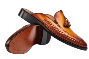 Crossed cognac handwoven tassel mules showing the burnished leather and brown underside