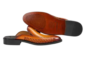 Brown leather outsole and dark heel top lift of a cognac woven tassel mule