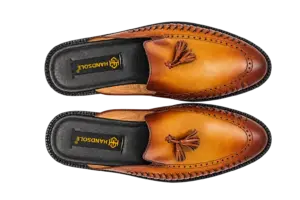 Overhead view of cognac backless tassel mules showing woven edges and HANDSOLE-branded footbeds