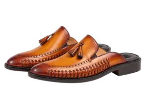 Three-quarter view of cognac tassel mules showing handwoven side panels and dark heel bases