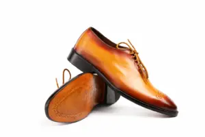 Crossed tan medallion-toe Oxfords showing the burnished upper and brown leather outsole