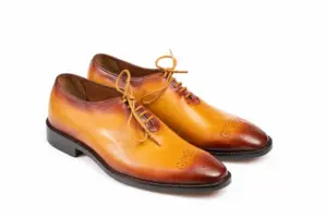 Three-quarter view of tan wholecut Oxford shoes showing closed lacing and toe medallions