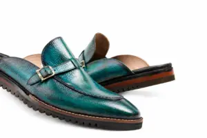 Close-up of teal patina buckle mules with Vibram soles showing silver-tone buckle, teal patina, apron seam and light sole-edge stitching