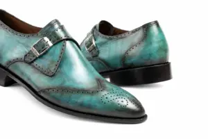 Close-up of turquoise patina wingtip single monk strap shoes showing single silver-tone buckle, wingtip broguing and turquoise tonal patina